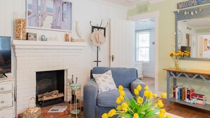 A cozy living room with a fireplace, a blue sofa, and a bookshelf. - Anna Maria Beach Cottage 110  Traditional beach cottage, moments from the sand! (Anna Maria)