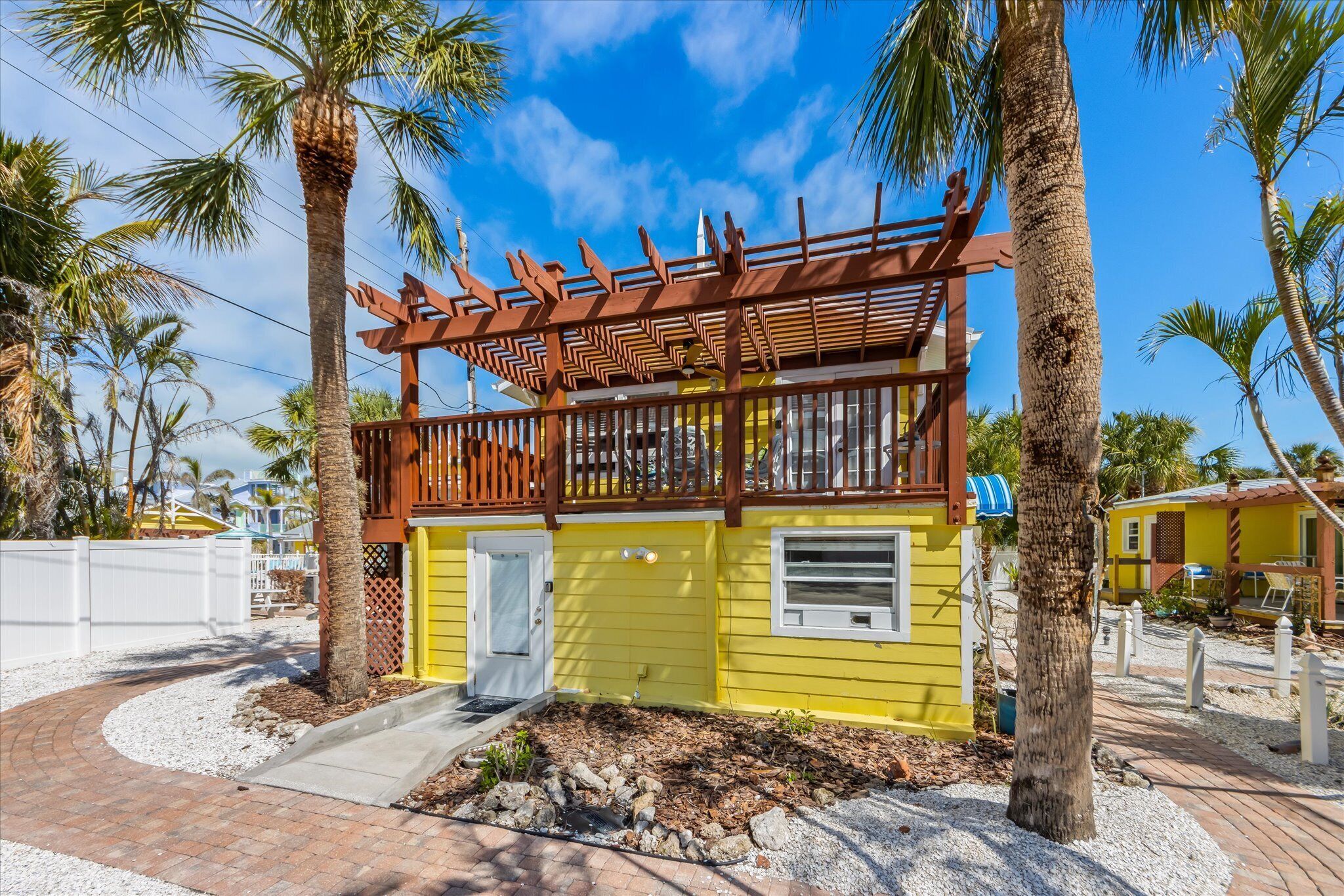 A two-story yellow building with a wooden balcony and a white door.