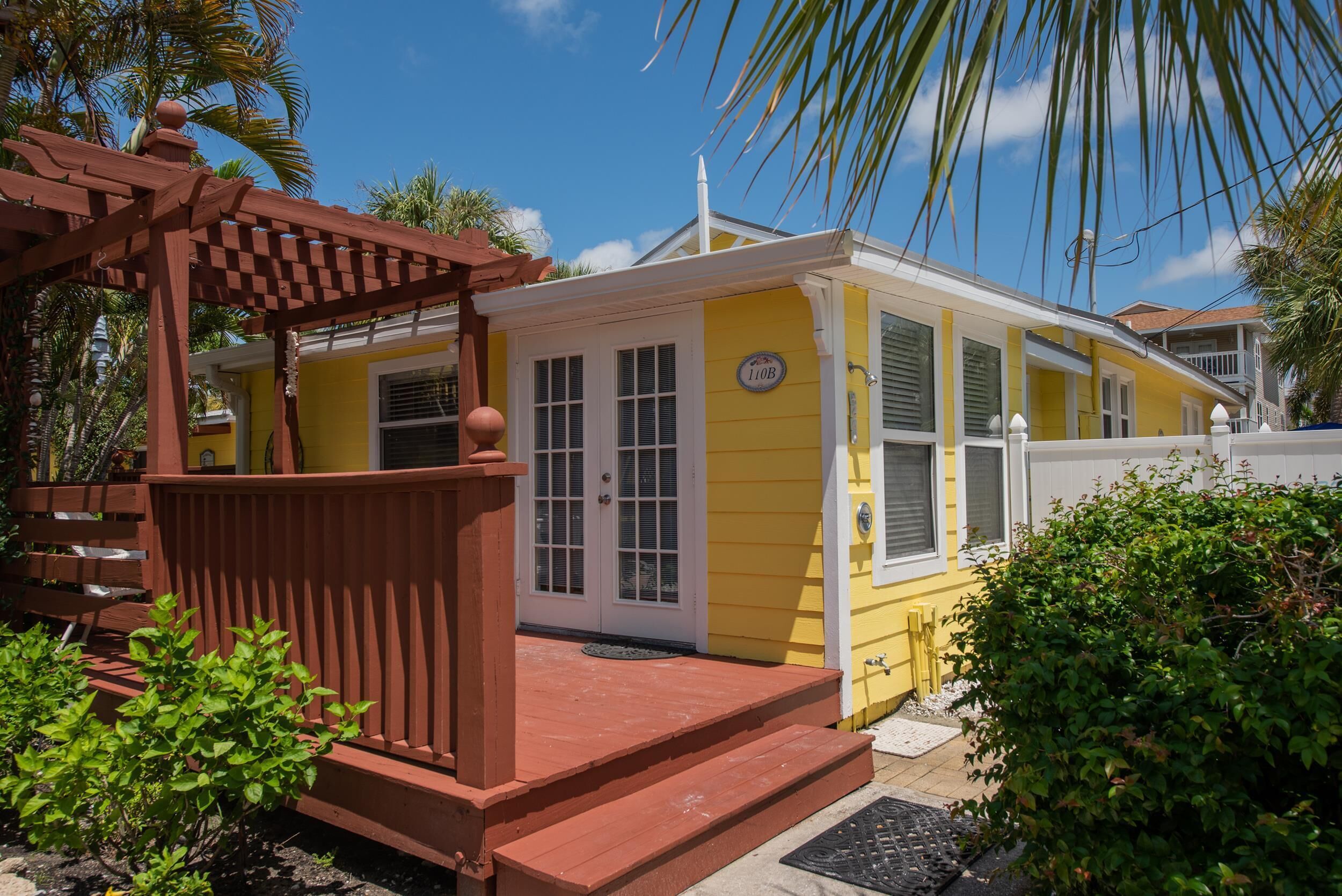 A yellow building with a porch and a wooden pergola.
