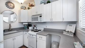 Una cocina con armarios blancos, microondas, estufa y fregadero. Hay adornos en los armarios y un cartel que dice 'recuerdos' sobre la encimera.