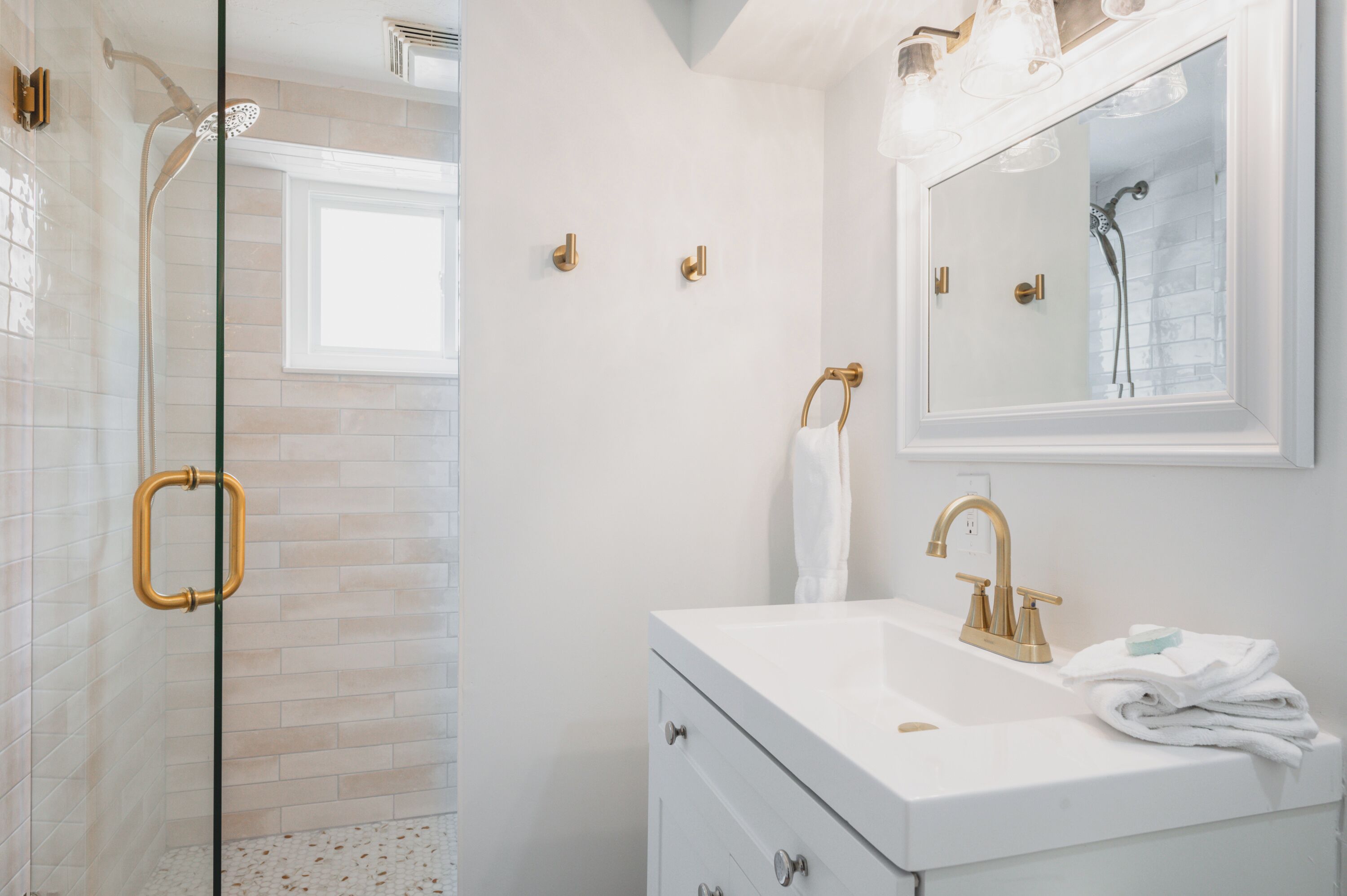 Une salle de bain moderne avec une douche à l’italienne en verre, un meuble-lavabo blanc avec un robinet doré et un grand miroir au-dessus du lavabo.