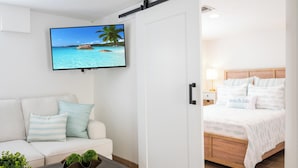 A hotel room with a bed, a TV on the wall, a sofa, and a coffee table. - Anna Maria Beach Cottage 110G  Updated beach cottage, with pool and beach gear! (Anna Maria)