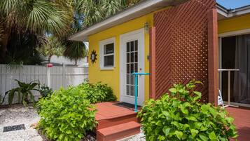 Un bâtiment jaune avec une porte rouge, une clôture en treillis de bois et des plantes vertes dans le jardin.