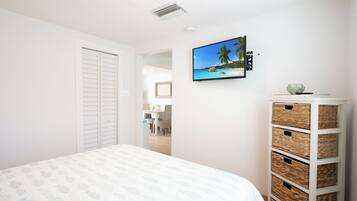 A bedroom with a bed, a TV on the wall, a white wardrobe, and a wicker storage unit.