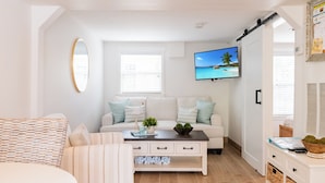 A modern living room with a sofa, a coffee table, and a television displaying a tropical beach scene. - Anna Maria Beach Cottage 110G  Updated beach cottage, with pool and beach gear! (Anna Maria)