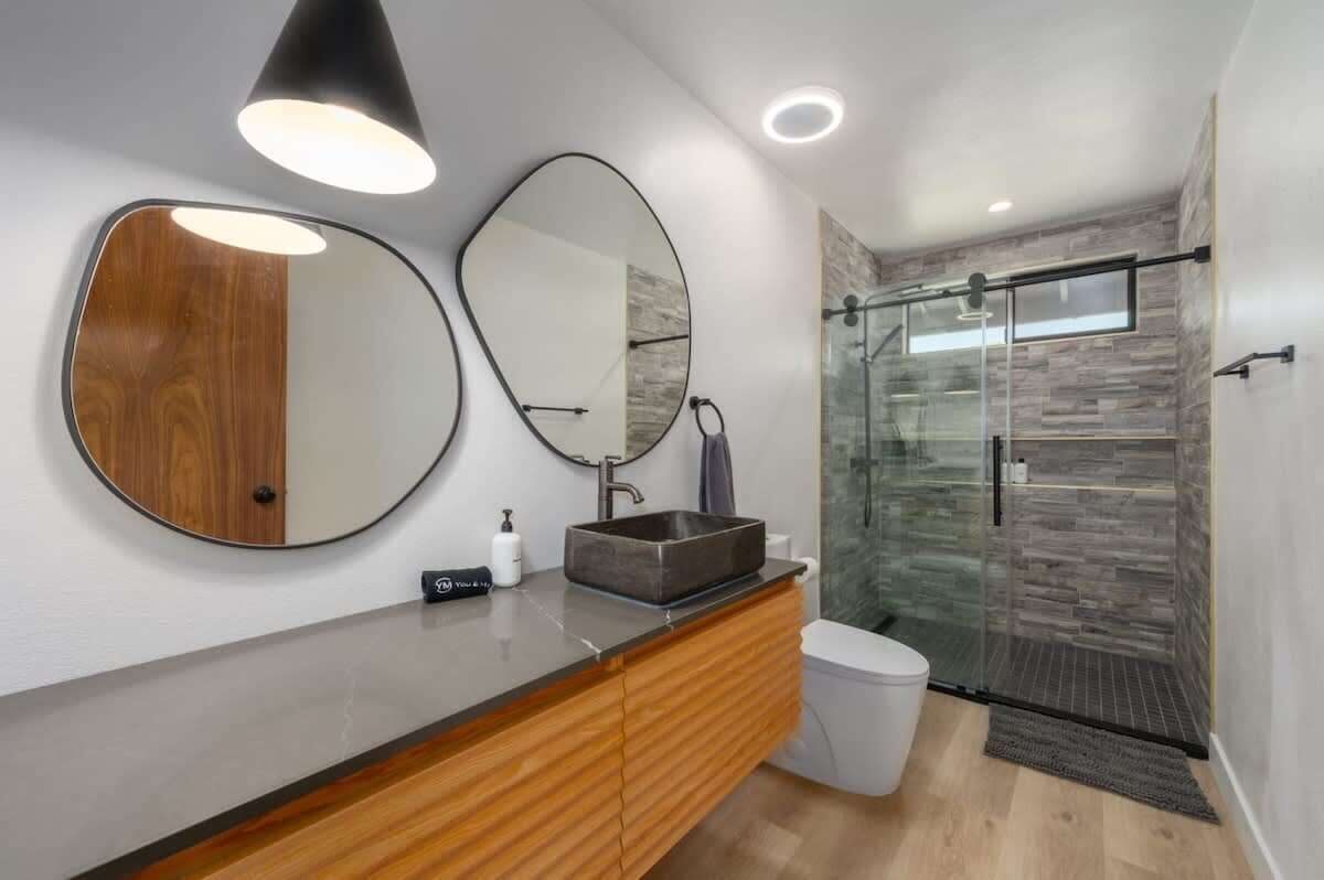 A modern bathroom with a wooden vanity, a large mirror, a glass shower enclosure, and a white toilet.