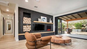 A modern living room with a fireplace, a round wooden table, and a comfortable armchair. - @ Marbella Lane - The Wine Mine Desert Escape (Joshua Tree)
