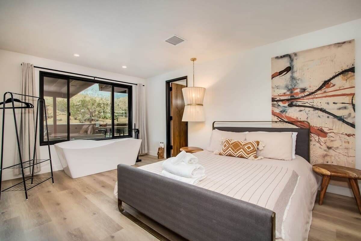 A modern bedroom with a large bed, a bathtub, and a view of the outdoors.
