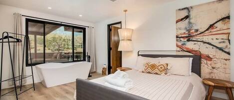 A modern bedroom with a large bed, a bathtub, and a view of the outdoors.