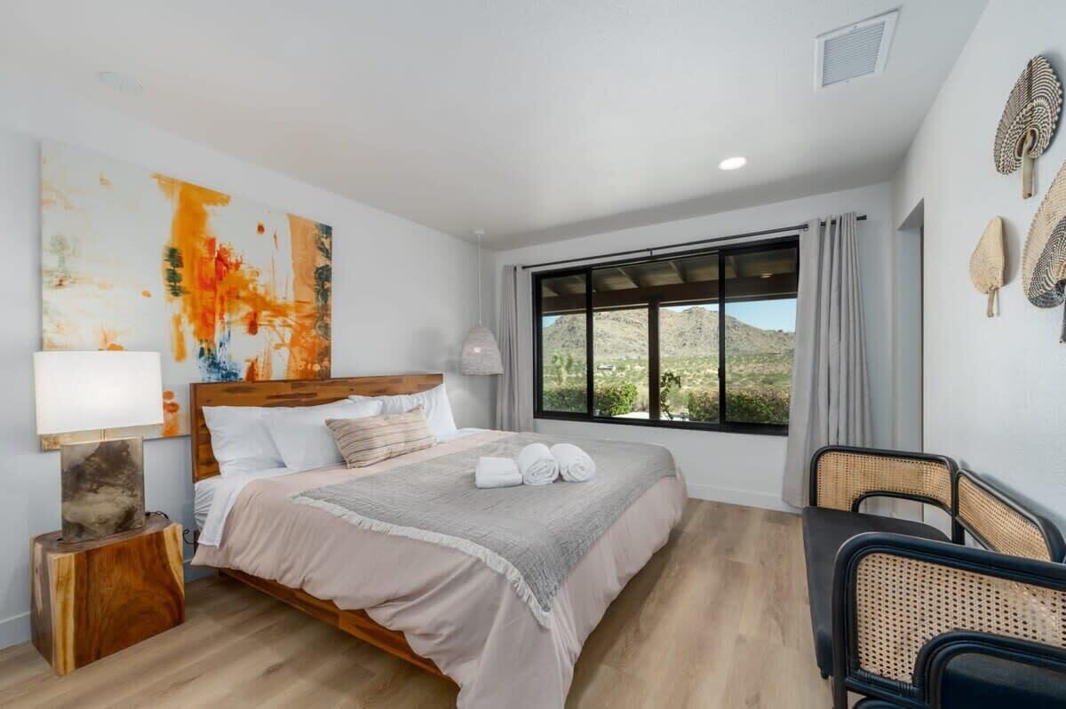 A bedroom with a large bed, a window with a view, a bedside table, and a chair.