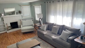 Un salon avec une cheminée, un canapé gris, une table basse en bois et un tapis à motifs.