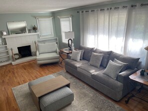 A living room with a fireplace, a grey sofa, a wooden coffee table, and a patterned rug. - Conviently located cozy 2 bedroom home on quiet street.  (Elkin)