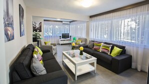 Moderni olohuone, jossa on kaksi sohvaa, sohvapöytä ja televisio. Ikkunoissa on verhot ja ikkunalaudalla kasvi.