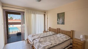 Quarto com cama, mesa de cabeceira, pintura e vista para uma piscina e roda gigante.
