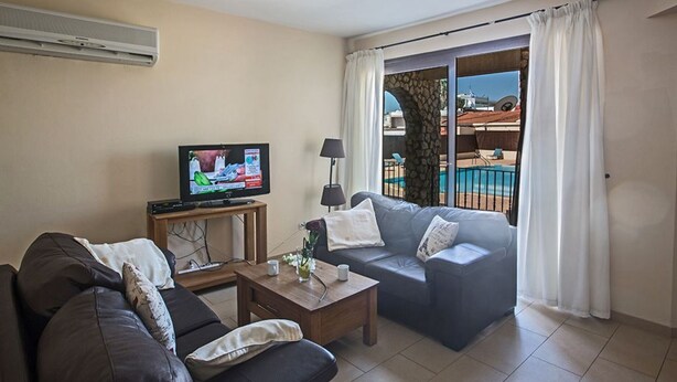 Sala de estar com televisão, sofá, mesa de centro e vista para uma piscina e um edifício.