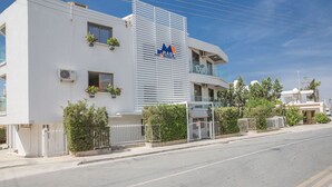 A modern building with a white facade, a logo on the side, and a gated entrance. - 5 Star Apartment for Rent in Cyprus, Ayia Napa Apartment 1325 (Ayia Napa)