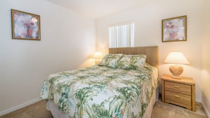Un dormitorio con cama, dos lámparas de noche, una mesita de noche y dos cuadros con motivos florales en las paredes.