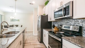 A modern kitchen with stainless steel appliances, a granite countertop, and a backsplash with a mosaic tile pattern. - 5 Star Villa Close to Disney Orlando Townhome 2676 (Kissimmee)