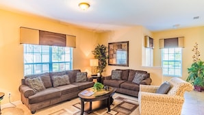 A living room with two sofas, a coffee table, and a wicker chair. There are large windows with blinds, a lamp, and a framed artwork on the wall. - Beautiful 5 Star Townhome on Paradise Palms Resort With Private Pool, Orlando Townhome 4833 (Kissimmee)