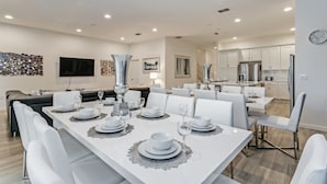 A modern dining area with a long table set for six, white chairs, and a large vase centerpiece. - Luxury 5 Star Villa on Solterra Resort,minutes From Disney World, Orlando Mansion 2750 (Davenport)