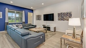 A modern living room with a blue accent wall, a grey sofa, a coffee table, a TV, and a decorative wall piece. - Luxury 5 Star Villa on Solterra Resort,minutes From Disney World, Orlando Mansion 2750 (Davenport)