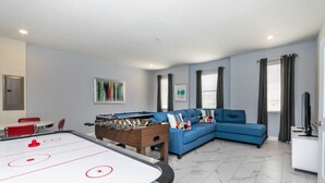 A living room with a foosball table, a blue sofa, and a television. - Luxury Mansion on Storey Lake Resort, Minutes From Disney World, Orlando Mansion 2672 (Kissimmee)