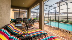 A covered patio area with wicker furniture and striped cushions, overlooking a swimming pool. - The Secret to Enjoying Your Luxury Villa Holiday on Windsor at Westside Resort, Orlando Villas 2806 (Kissimmee)