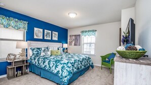 A bedroom with a blue accent wall, a bed with a tropical print bedspread, a green chair, and a wooden nightstand with decorative items. - The Secret to Enjoying Your Luxury Villa Holiday on Windsor at Westside Resort, Orlando Villas 2806 (Kissimmee)