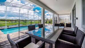 Un balcón acristalado con piscina, mobiliario de mimbre y vistas a un paisaje verde.
