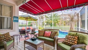 A covered outdoor area with wicker furniture, a glass table, and a pool view. - Luxury 5 Star Villa on Highlands Reserve Resort, Orlando Villa 2748 (Davenport)