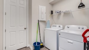A laundry room with a washing machine, dryer, and a shelf with cleaning supplies.