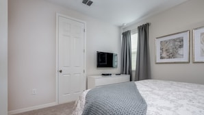 A bedroom with a bed, a TV on a stand, a door, and a window with curtains.