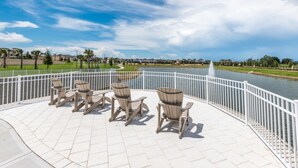 An outdoor seating area with Adirondack chairs and a view of a lake and park.