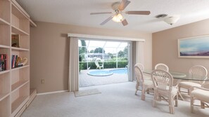 A room with a glass table and chairs, a ceiling fan, a bookshelf, and a view of a swimming pool outside. - 5 Star Villa on Charlotte Harbor, Charlotte County Villa 1011 (Punta Gorda)