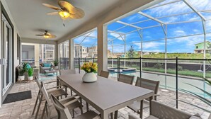 A covered patio with a table and chairs, a ceiling fan, and a view of a swimming pool and houses. - 5 Star Villa on Champions Gate Resort With First Class Amenities, Orlando Villa 3218 (Kissimmee)