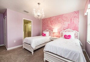 Une chambre avec deux lits, un lustre et un mur décoré dans des tons roses.