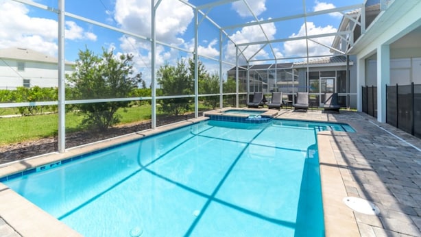 Una piscina con cerramiento de vidrio, rodeada por una terraza con sillas de descanso.