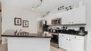 A modern kitchen with white cabinets, a granite countertop, stainless steel appliances, and decorative wall art. - The Ultimate 5 Star Villa With Private Pool on Windsor Hills Resort, Orlando Villa 4855 (Kissimmee)