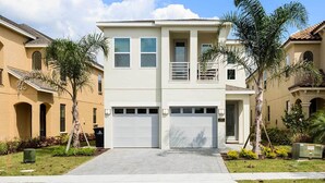 A two-story residential building with a central garage, a balcony on the upper floor, and a small front yard with palm trees and shrubs. - 5 Star Villa With Private Pool on Reunion Resort and Spa, Orlando Villa 4591 (Kissimmee)