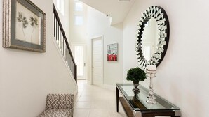 A hallway with a staircase, a bench, a glass-top console table with a decorative item, a mirror with a unique frame, and a framed picture on the wall. - 5 Star Villa With Private Pool on Reunion Resort and Spa, Orlando Villa 4591 (Kissimmee)