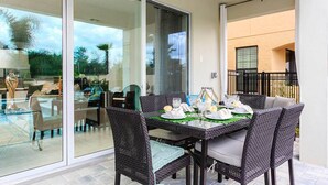 An outdoor dining area with wicker chairs and a glass table set for two, overlooking a garden. - 5 Star Villa With Private Pool on Reunion Resort and Spa, Orlando Villa 4591 (Kissimmee)