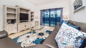A living room with a sofa, a glass coffee table, a TV on a cabinet, and a view of the outdoors through a window. - The Ultimate 5 Star Villa With Private Pool on Windsor Palms Resort, Orlando Villa 5026 (Kissimmee)