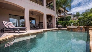 A pool area with lounge chairs, a covered patio, and a two-story building with balconies. - 5 Star Villa on Orlandos Most Exclusive Reunion Resort and Spa, Orlando Villa 4599 (Kissimmee)