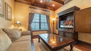 A living room with a sofa, a glass-top coffee table, a television on a wooden stand, and a window with curtains. - 5 Star Villa on Orlandos Most Exclusive Reunion Resort and Spa, Orlando Villa 4599 (Kissimmee)