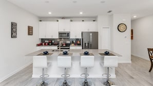 Een moderne keuken met witte kasten, roestvrijstalen apparatuur en een centraal eiland met barstoelen.