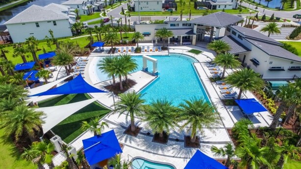 Un resort con una gran piscina central, varias piscinas más pequeñas y un paisaje bien cuidado con palmeras y sombrillas azules.