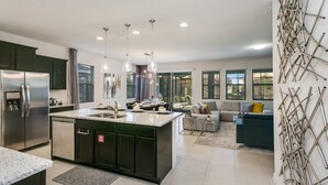 Eine moderne Küche mit Kochinsel, Edelstahlgeräten, Pendelleuchten und einem Essbereich mit Sofa und Couchtisch.