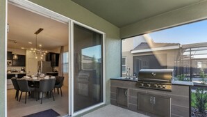 Eine moderne Küche mit einer Schiebeglastür, die zu einem Essbereich führt, einem eingebauten Grill und Blick auf ein Nachbarhaus.