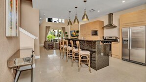 A modern kitchen with a central island, bar stools, pendant lighting, and a stainless steel refrigerator. - 5star Villa Close to Disney, Orlando Townhome 3701 (Kissimmee)