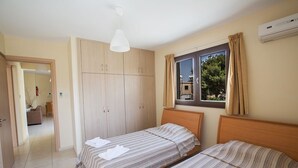 A bedroom with two single beds, a wardrobe, a window with curtains, and an air conditioning unit. - Beautiful Apartment With Communal Pool, Ayia Napa Apartment 1282 (Ayia Napa)